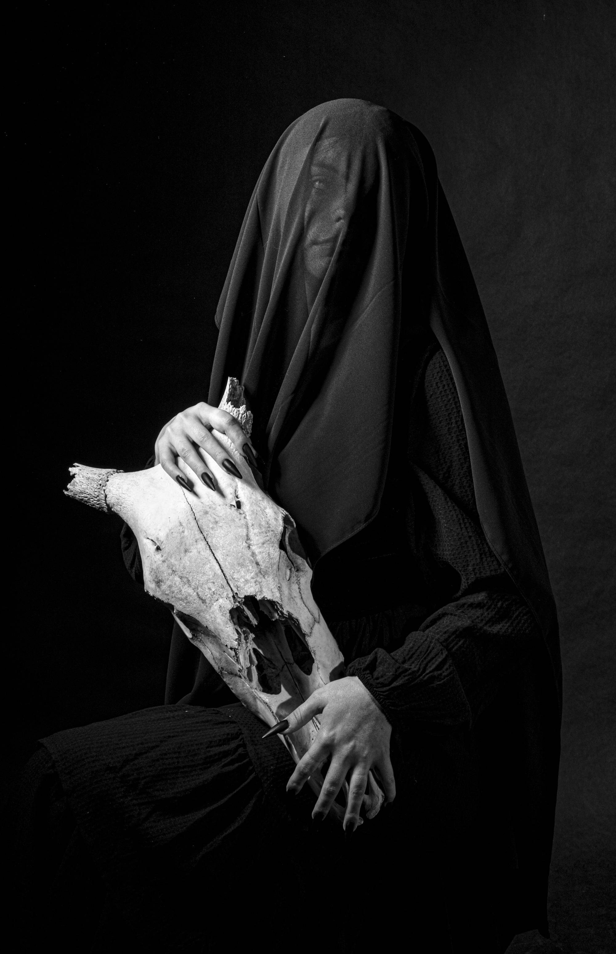 Black and white photograph of a person covered in black fabric holding a skull.